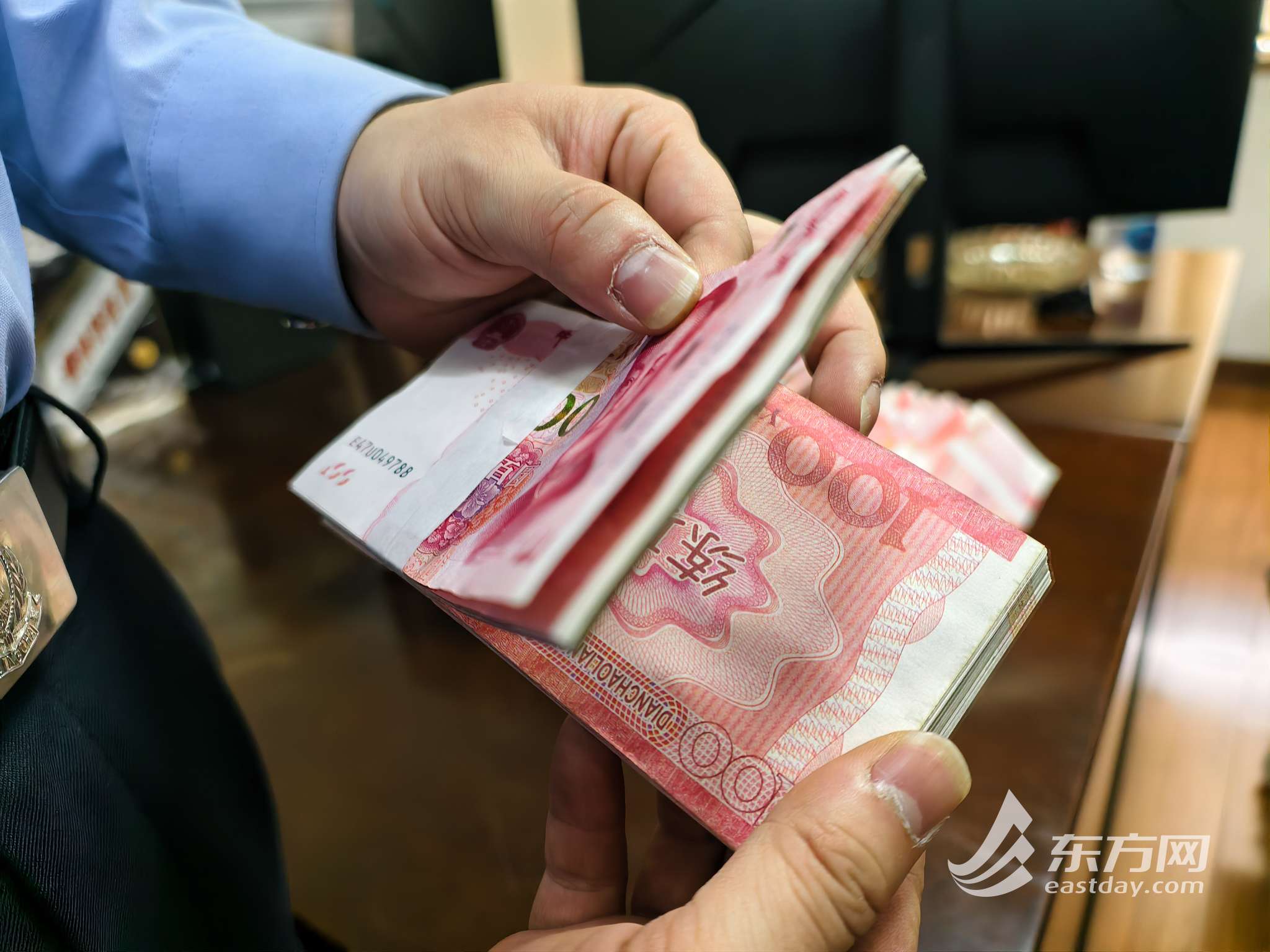 图为民警向记者展示犯罪嫌疑人为更好掩人耳目,每捆钱的首张和末张百元币使用真钞,其余百元面额均为“练功券”(蔡黄浩/摄)