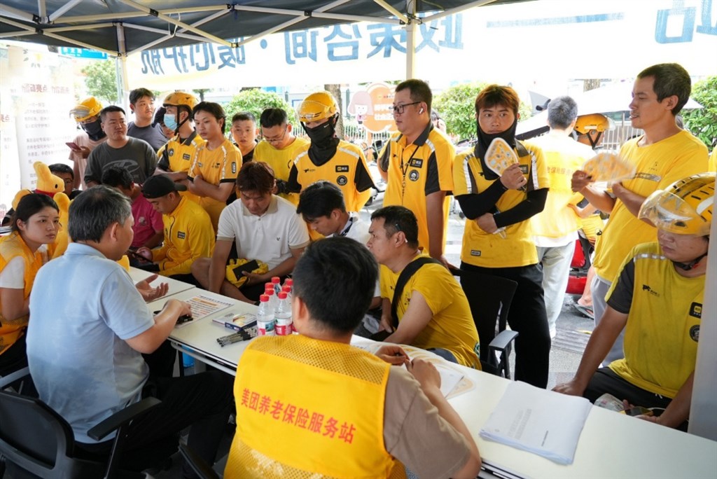 骑手在街头服务站向人社部门工作人员咨询养老保险参保流程。